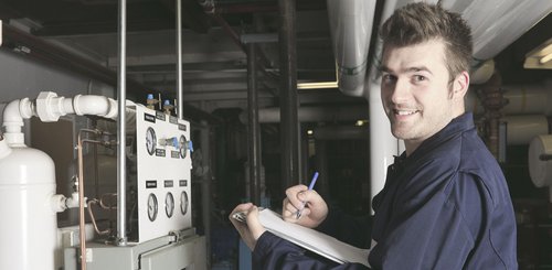 Ein Anlagenmechaniker vor einer Heizungsanlage, der ein Klemmbrett hält